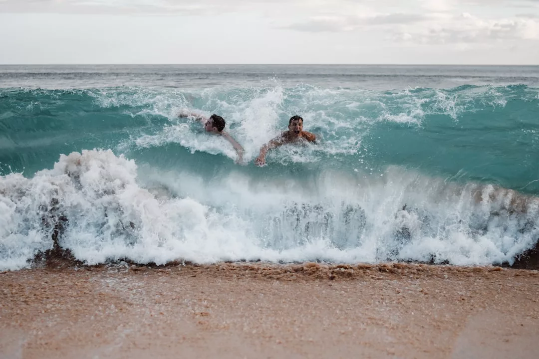 Dos personas quedan atrapadas en una ola rompiente cerca de la orilla en una hermosa playa de Mallorca, con el agua chapoteando a su alrededor y la playa de arena en primer plano.