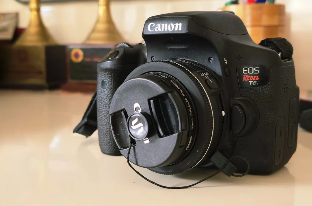 Una cámara DSLR Canon EOS Rebel T6i con una tapa de objetivo descansa sobre una superficie blanca; unos trofeos difuminados al fondo evocan el lujo y el prestigio de los mejores momentos de Mallorca.