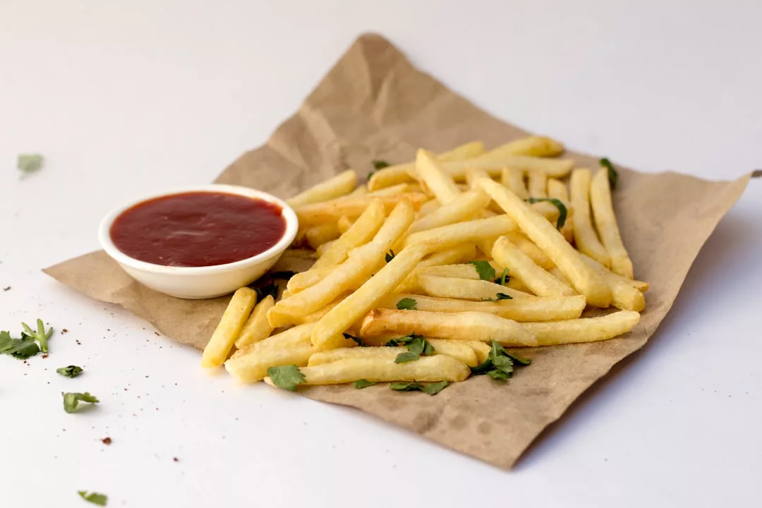 Las patatas fritas esparcidas sobre papel de estraza con un pequeño cuenco de ketchup y unas cuantas guarniciones de hierbas verdes evocan un lujo desenfadado, perfecto para disfrutar del sabor de Mallorca.