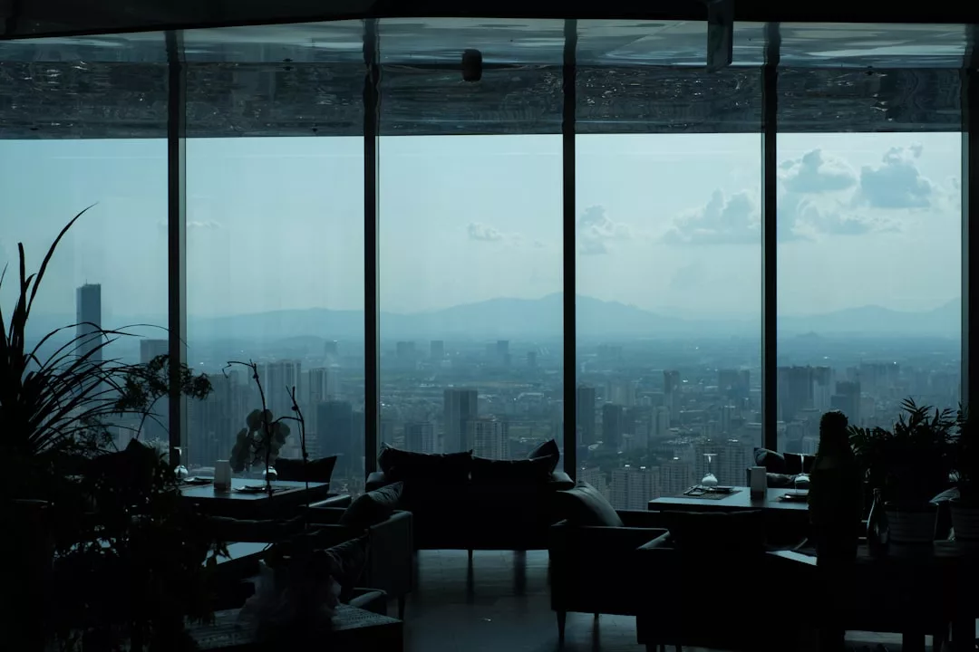 Interior del restaurante Lujo, tenuemente iluminado, con grandes ventanales que dan a un paisaje urbano de Mallorca y a montañas lejanas bajo un cielo nublado.
