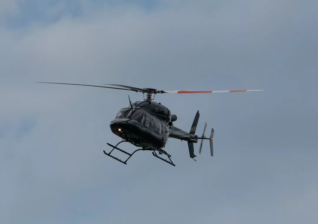 Un helicóptero negro con marcas blancas y naranjas en su rotor de cola se eleva sobre el cielo nublado de Mallorca, ofreciendo un toque de lujo a la vista panorámica.