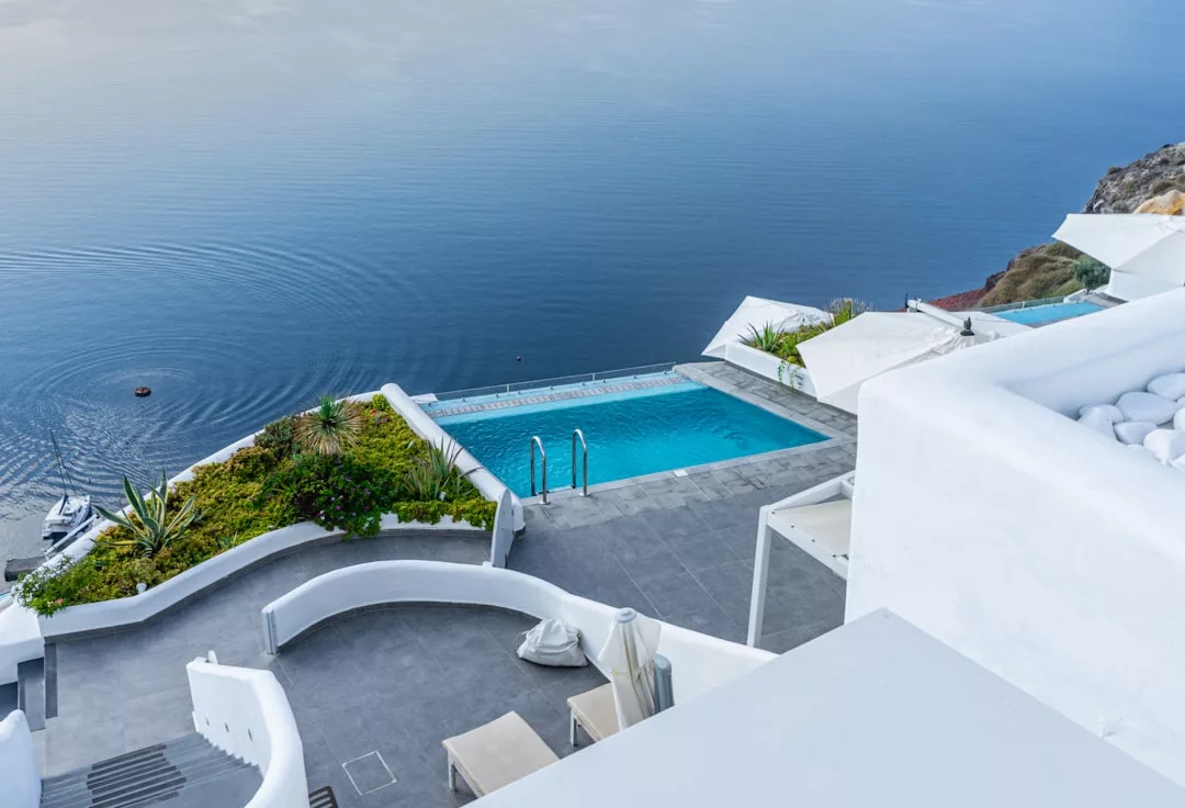 Una piscina Lujo con tumbonas blancas domina un mar tranquilo desde una moderna terraza de paredes blancas en una ladera de Mallorca.