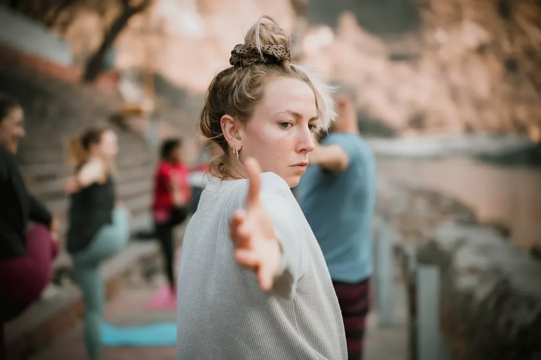Una mujer estira el brazo hacia delante en una sesión de yoga al aire libre en Mallorca, exudando una sensación de lujo mientras otros participantes practican en el pintoresco fondo.