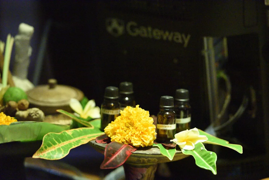 Pequeños frascos de aceites esenciales se exponen en una bandeja con flores y hojas, evocando el lujo y la belleza natural de Mallorca, con un ordenador Gateway visible al fondo.