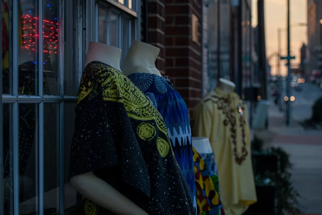 Tres maniquíes vestidos con coloridas prendas estampadas destilan lujo mientras se exhiben en el exterior de un elegante escaparate mallorquín al atardecer en una animada calle de la ciudad.