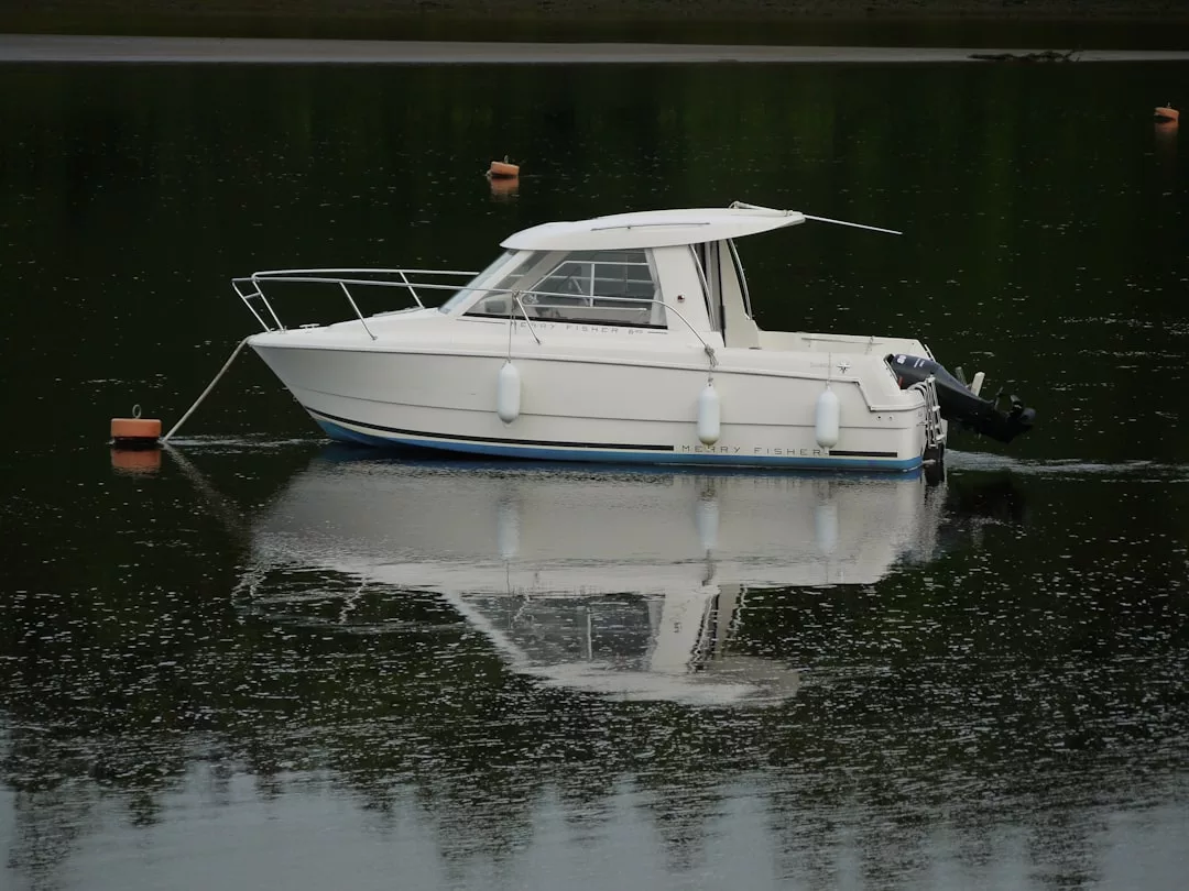 Una pequeña lancha blanca con cabina está anclada en las tranquilas aguas de Mallorca, reflejando su imagen en la superficie. Unas boyas naranjas flotan cerca, realzando la sensación de lujo y tranquilidad.