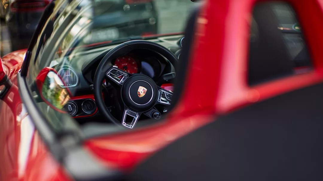 Primer plano del interior de un deportivo Porsche rojo, que muestra lujo y elegancia en el diseño, con especial atención al volante y al salpicadero vistos a través de la ventanilla lateral del conductor en Mallorca.
