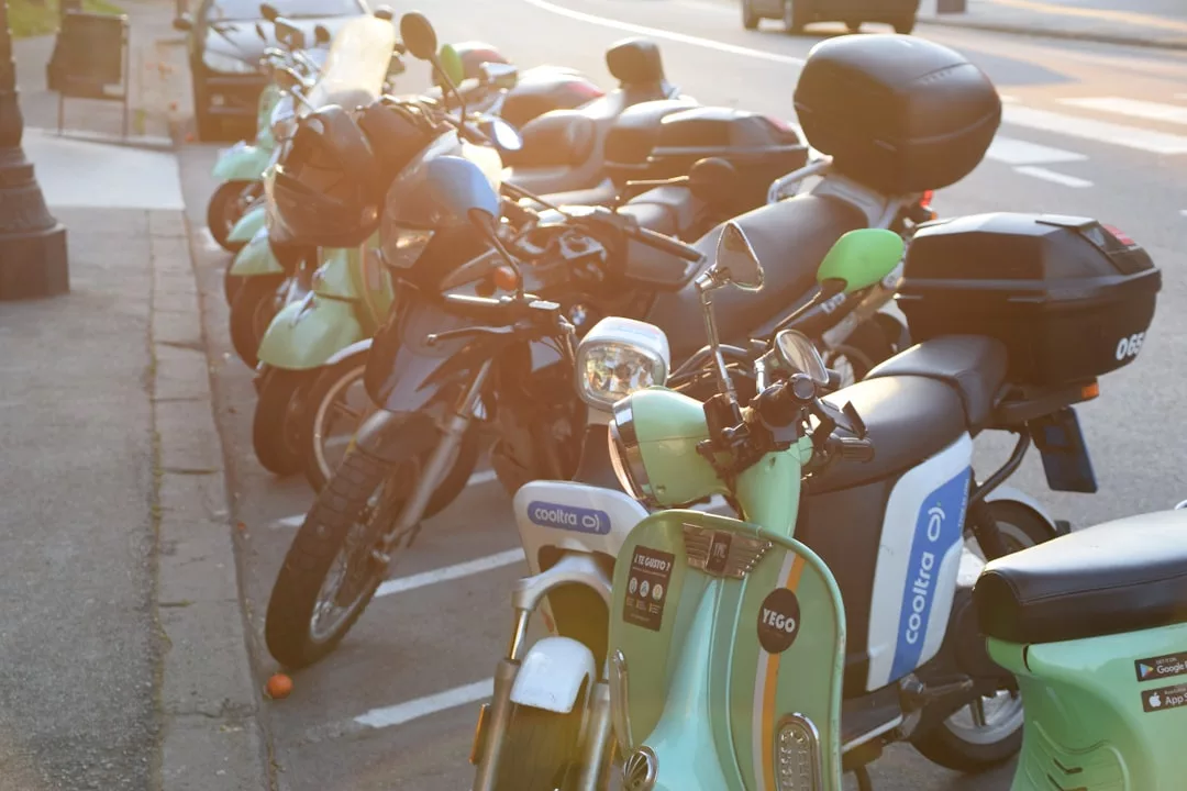 Fila de scooters y motocicletas aparcadas en un aparcamiento al aire libre iluminado por el sol junto a una calle de Mallorca.