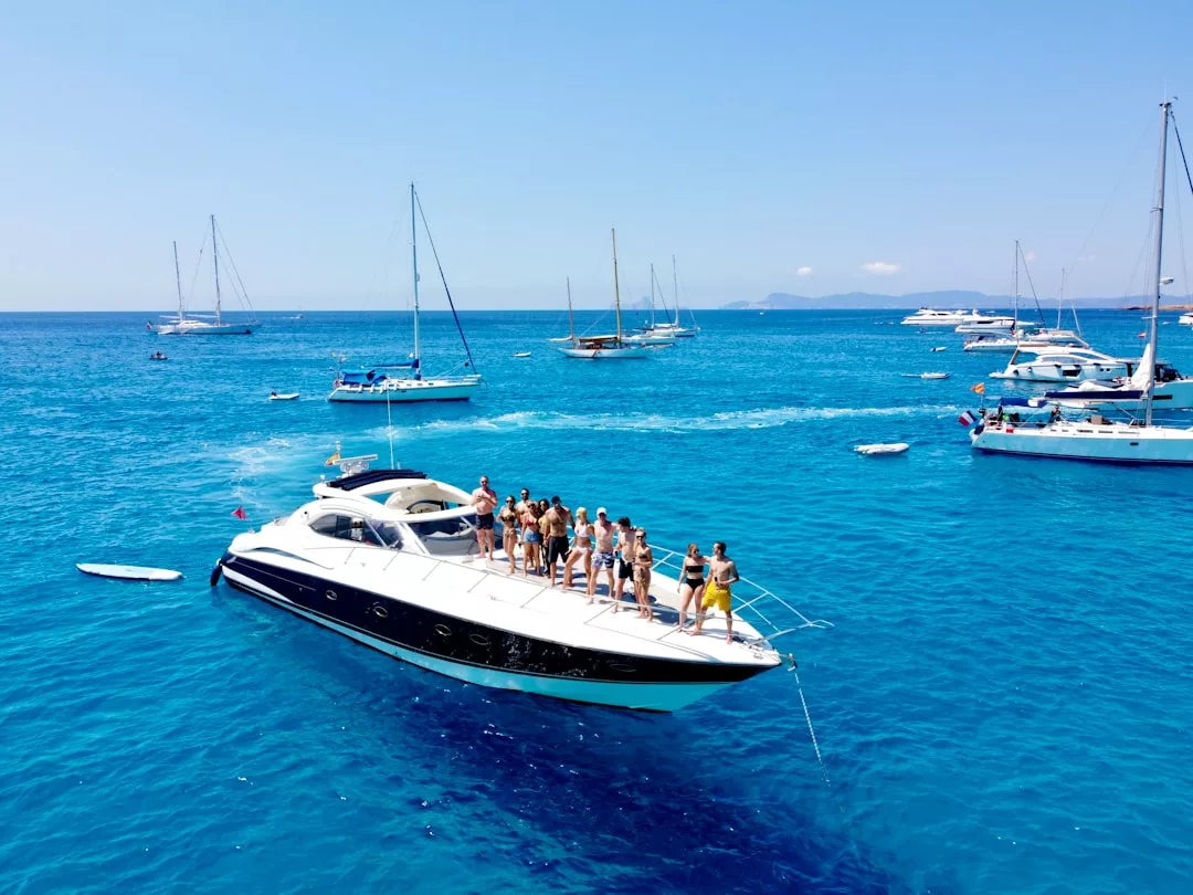 Un grupo de personas se encuentra en la cubierta de un yate a motor de lujo en aguas cristalinas de Mallorca, rodeado de otras embarcaciones bajo un cielo soleado.