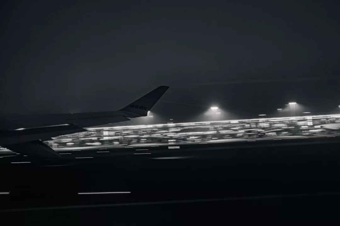El ala de un avión se ve contra una terminal de aeropuerto de Mallorca tenuemente iluminada por la noche, con luces de pista borrosas que indican movimiento y un toque de lujo en el ambiente sereno y exclusivo.